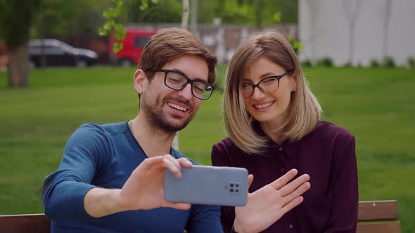 Happy couple wearing eye glasses waving hands at camera during video chat.