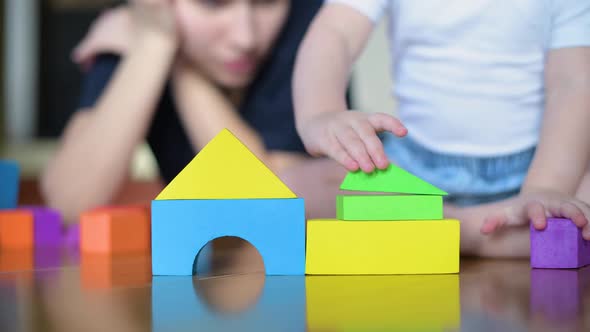 A small child neatly builds a tower of colored figures on the floor under the supervision