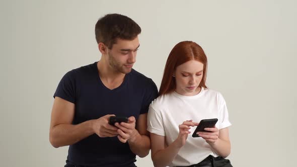 Studio Portrait of Young Man Showing Fun Video on Smartphone to Happy Girlfriend Standing on White