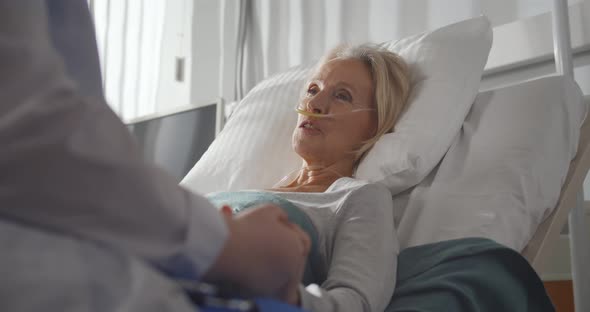 Close Up of Doctor Holding Hand and Talking To Sick Aged Female Patient in Hospital Ward