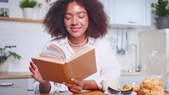 Attractive African American Woman Leafs Through Pages of Book and Smiles