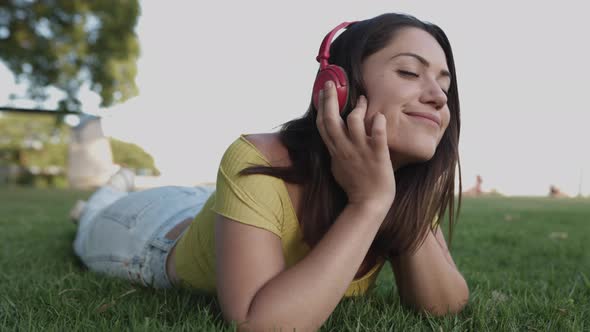 Young Hispanic Woman Listening to Music with Headphones While Relaxing on Green Grass at Park