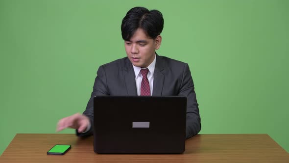 Young Handsome Asian Businessman Working with Laptop Against Green Background