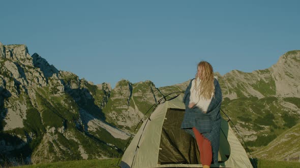 Happy travel woman with dreadlocks near the tent standing on top of hill looking at sunrise.