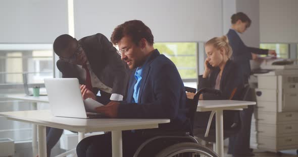 Male Office Worker in Wheelchair Holding Document and Discussing with Colleague