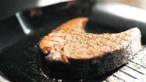 A Salmon Fillets on a Grill Plate is Sprinkling Spices