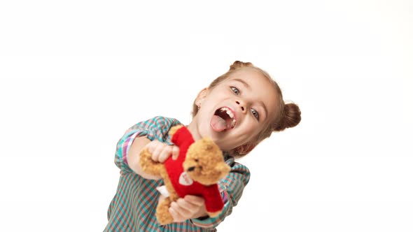 Young Adorable Caucasian Kid Girl with Two Hair Buns Showing Small Teddy Bear Smiling Making Faces