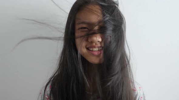 Slow motion shot of Happy Asian girl playing with hair blowing on white background.