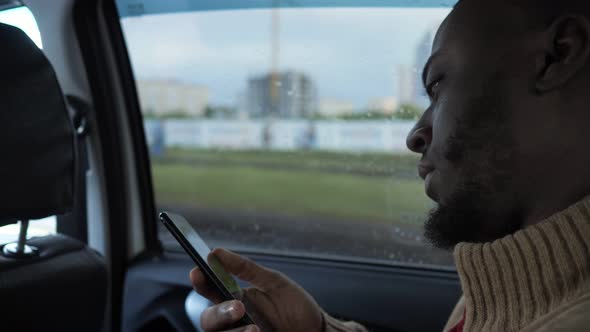 Portrait of Black Man Browsing Smartphone Is Riding a Car in Rainy Day in City