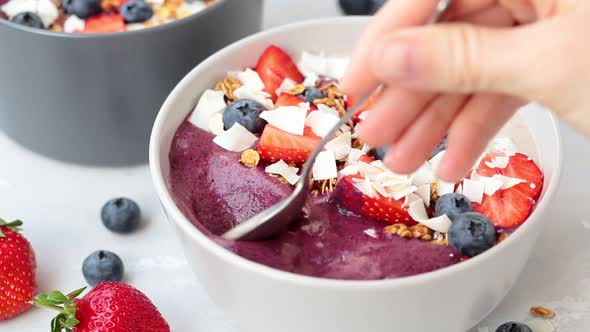 Eating with Spoon Berry Smoothie Bowl with Granola, Strawberries, Blueberries and Coconut. 