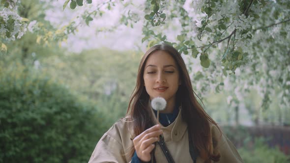 Young female blowing into dandelion while looking into the camera