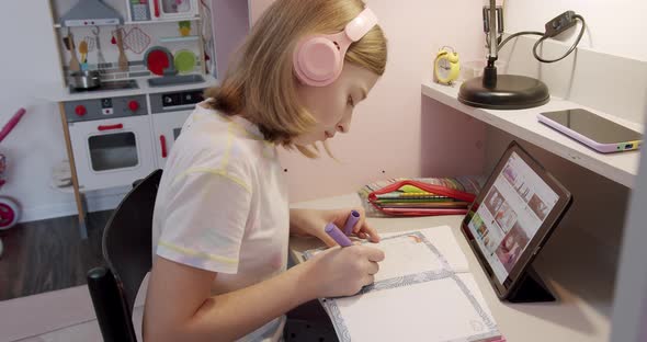 Teenager with Headphones Writes on Notebook and Uses Tablet Gadget for Internet