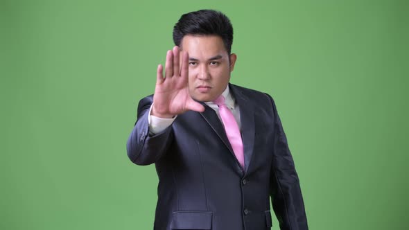 Young Handsome Overweight Asian Businessman Against Green Background