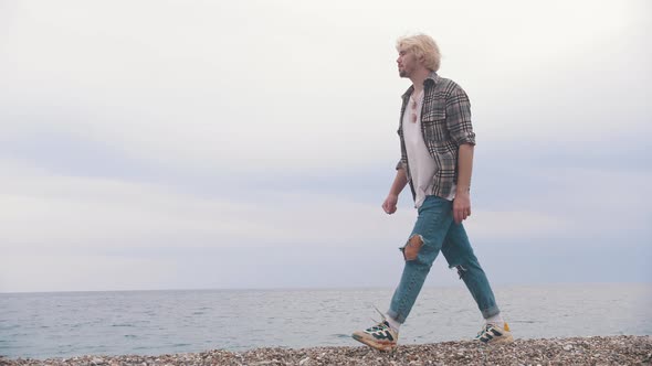 A Young Blonde Man Walks on the Shore By the Sea