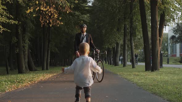 Baby Running to Meet His Dad After Work Businessman with Bicycle at City Park