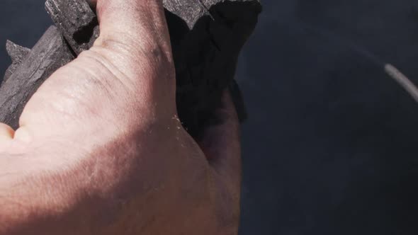 Man's hand inserting pieces of charcoal into a barrel for roasting