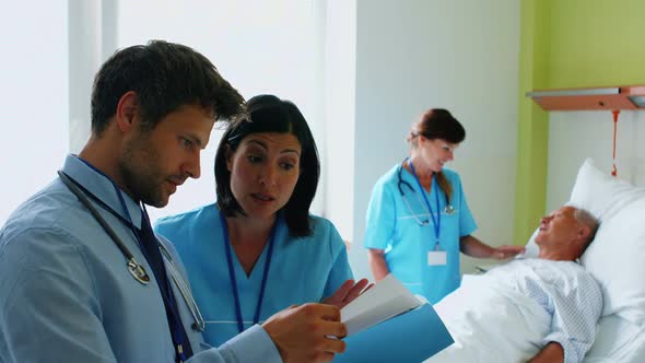 Doctors discussing on reports while nurse interacting with patient in background