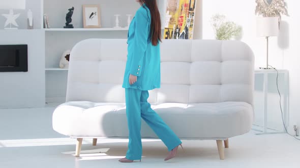 Young Woman in Blue Blazer Sits Down on the Couch in White Studio