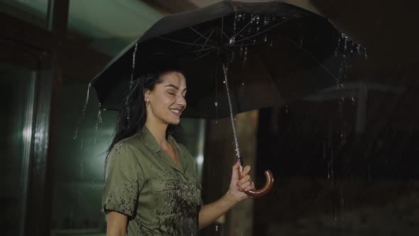 Happy Girl with Umbrella in Hand Smiling Under the Night Rain