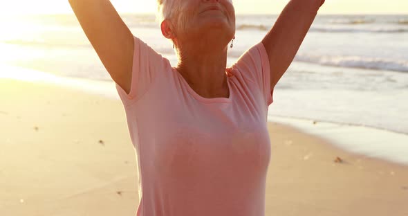 Senior woman standing with arms outstretched on beach