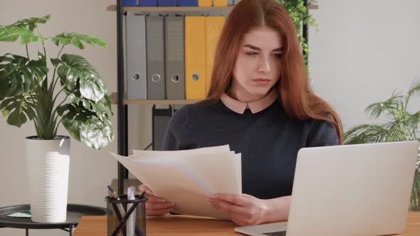 red hair female student reading documents, analyzing financial papers, preparing audit report at wor