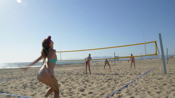 Women players play beach volleyball and a player jump serves serving the ball.