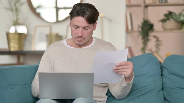 Middle Aged Man with Documents Working on Laptop , at Home