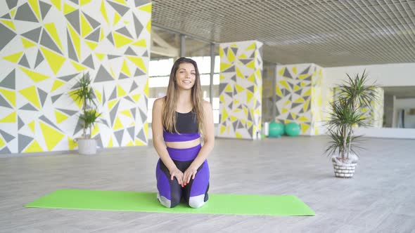 Athletic Female Tabata Coach Kneeling on Green Mat in Gym Doing Online Fitness Class