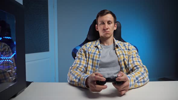 Young Man Plays Computer Game with Gamepad in Semidark Room