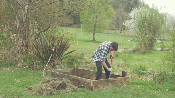 WIDE SHOT of young man ring top soil with shovel building raised garden bed