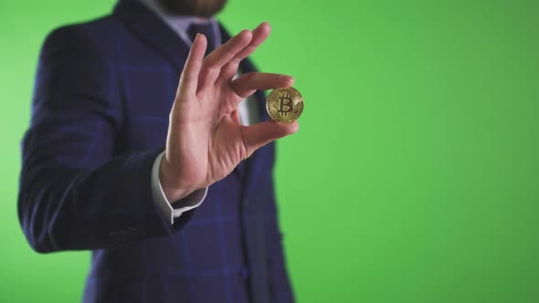 Bearded Businessman Holding Bitcoin in Hand Standing on Green Background in Office.