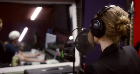 Caucasian Woman Stands with Her Back and Sings a Song in a Recording Studio