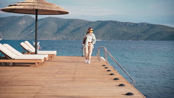 Woman Traveler in a Mask on His Face Walks on a Wooden Sea Pier, Summer Travel