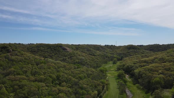 Scenic valley with golf course at the bottom. Blue sky with wispy clouds about the treetops.