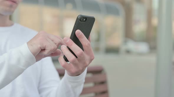 Close Up of Young Man Using Smartphone While Sitting Outdoor on Bench
