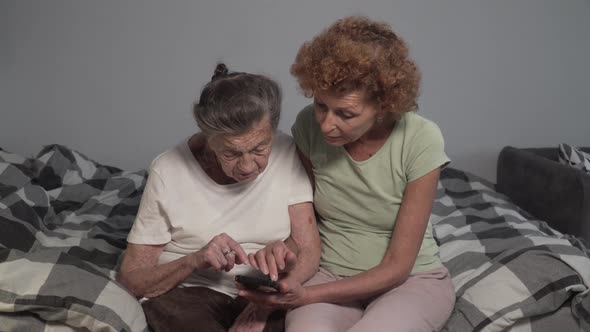 Happy Middle Aged Woman Hugs Senior Mom, Showing How To Use Mobile Apps. Smiling Elderly Mother