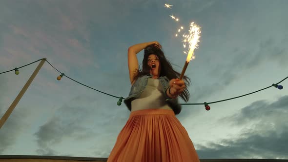 Low angle view of woman jumping with firework candle on rooftop terrace