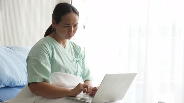 Sick Asian woman using laptop while staying at hospital room.