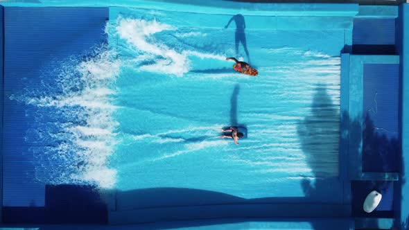 Guys rides a surfboards on an artificial wave in wave pool machine.