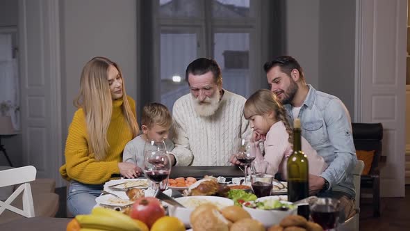 Grandfather Opening Computer on the Dinner Table and Watching on Photos with His Family