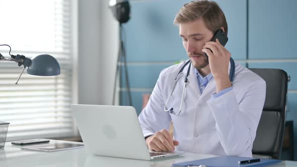 Doctor Talking on Smartphone While Working on Laptop