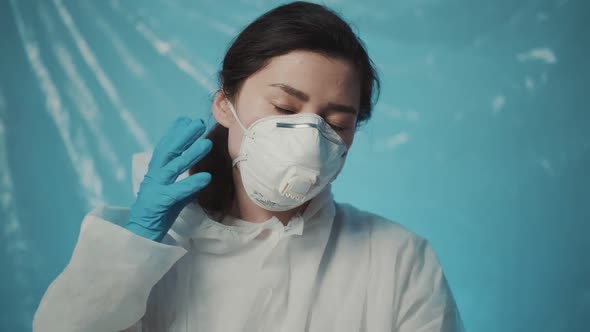 Tired but Happy Female Doctor Nurse in Protective Costume Taking Off Mask and Glasses After Long Day