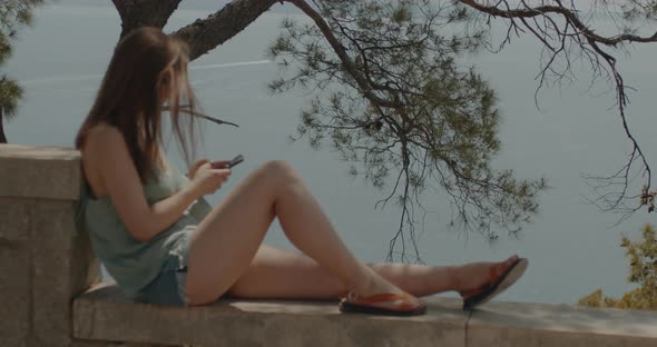 Young woman lies on the stone railing and navigates on her smartphone