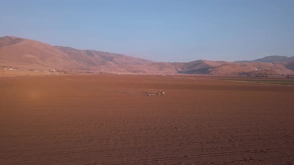 Aerial, Tractor in distance plowing field with California mountain background