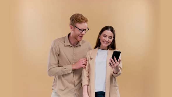 Man and Woman Holding Smartphone and Smiling at Each Other Positive Online Communication Over Beige