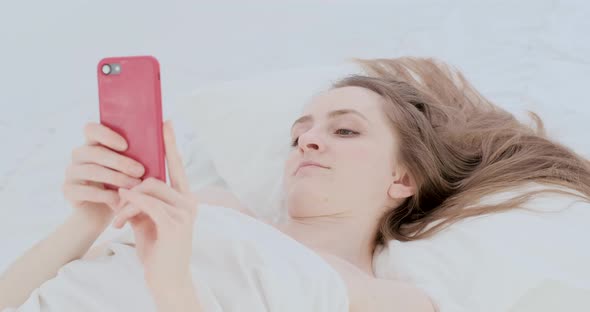 Beautiful Young Woman in Bed with Phone in Her Hands Writes Messages