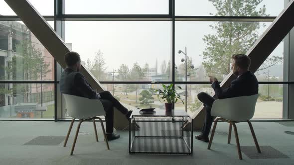 Two Businessmen Sitting on Couches and Discussing at Coffee Table