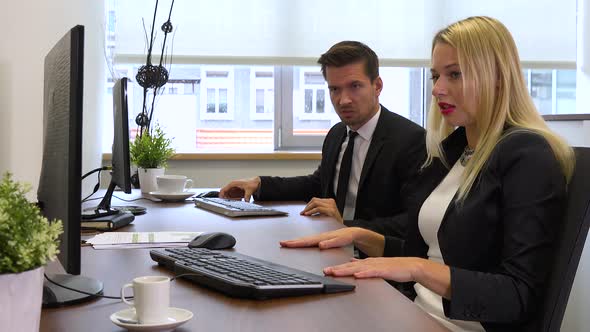 Two office workers, man and woman, look at a computer on a desk and get angry