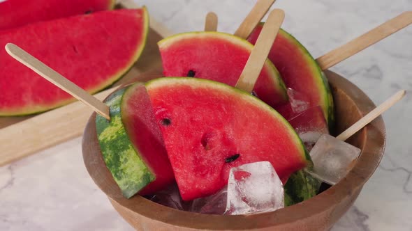 Watermelon slices on sticks with ice cubes. Fresh watermelon popsicles in wooden bowl.