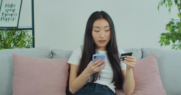 Young Asian Woman Holding a Credit Card Using a Mobile Phone to Making an Online Payment